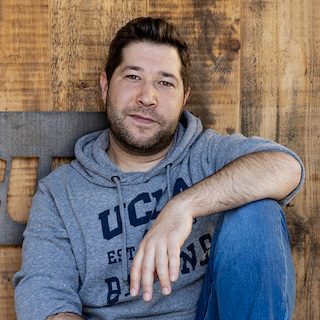 Porträtaufnahme von Dennis Ramin vor einer Holzwand