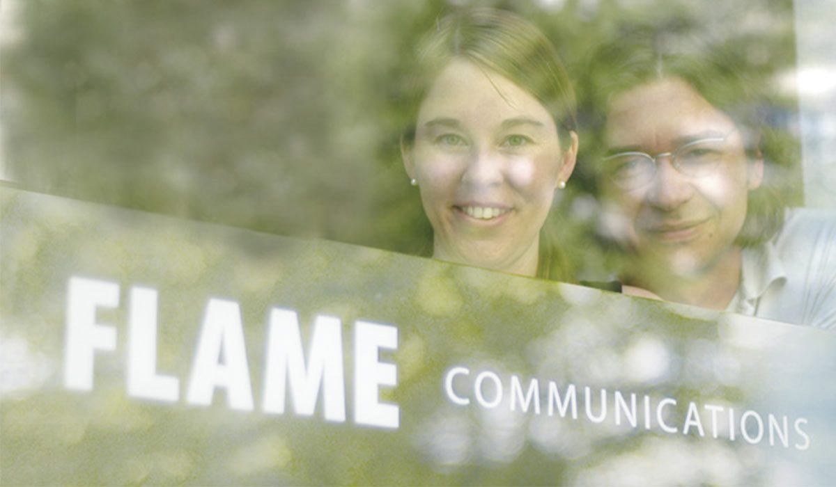 Petra und Boris hinter der Glastür mit dem Schriftzug flame communications