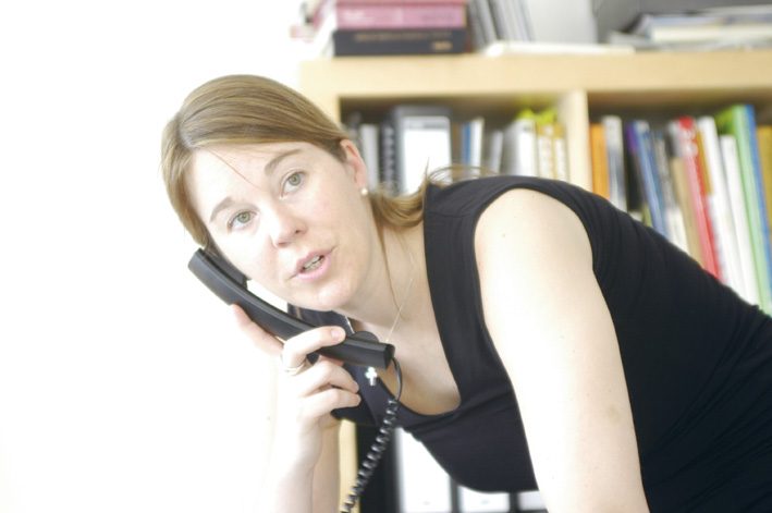 Petra telefoniert an ihrem Schreibtisch vor einem Bücherregal